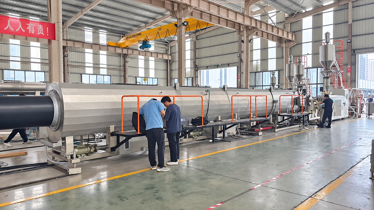 Operators working beside a long stainless steel pipe-processing tank with red safety rails