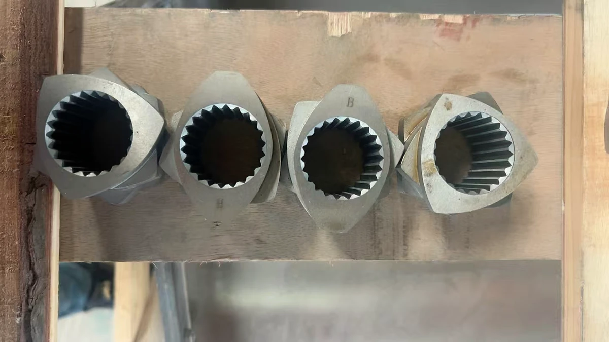 Four metal screw elements with internally splined bores arranged in a wooden container.