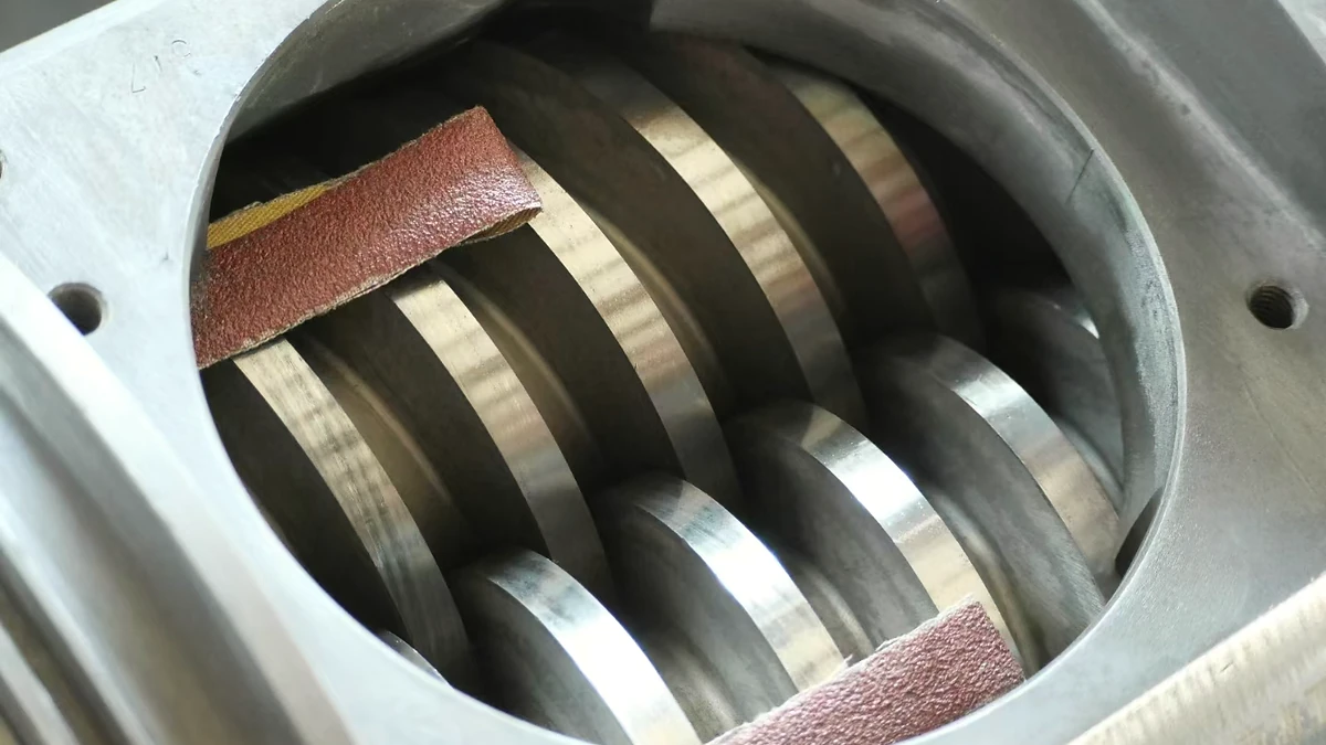 Two extruder screws visible through the feed opening of a conical twin-screw barrel.