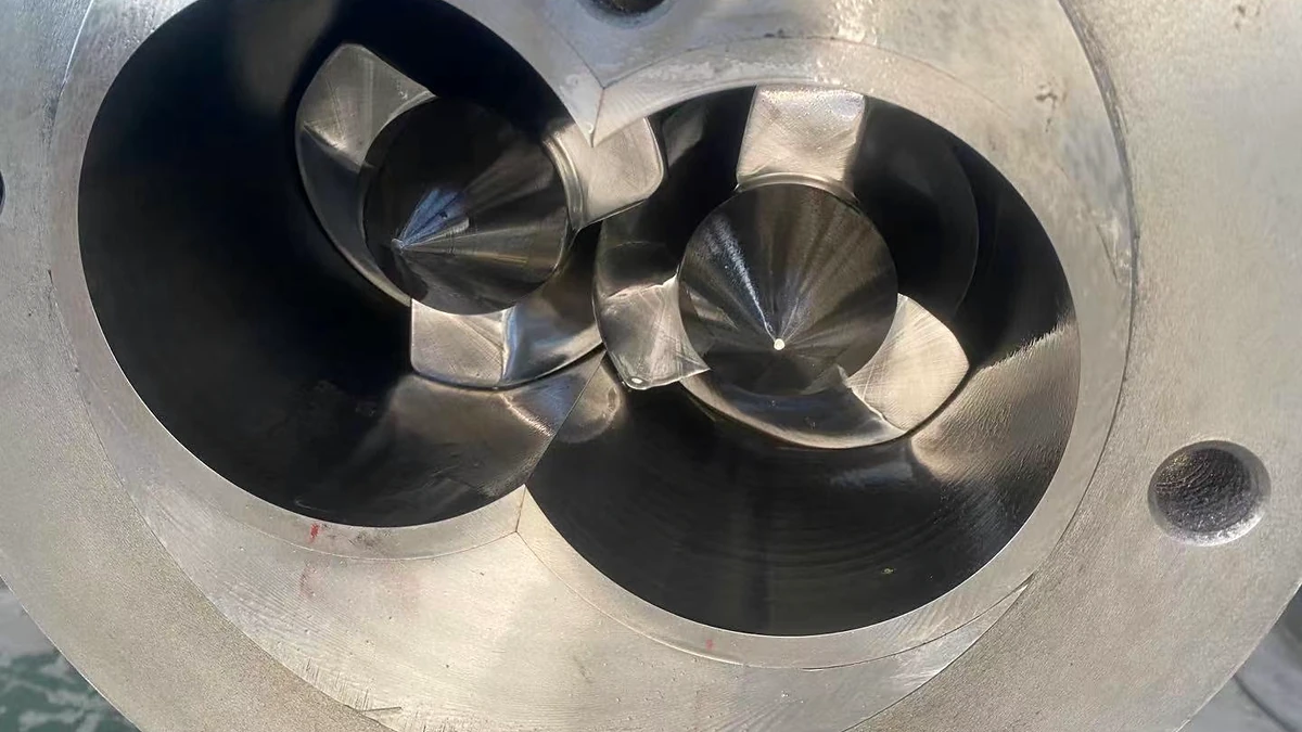 Two polished screw tips visible inside the end face of a twin-screw barrel.
