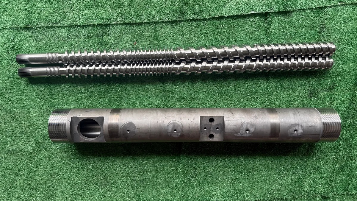 Two parallel extruder screws displayed above a matching twin-screw barrel.