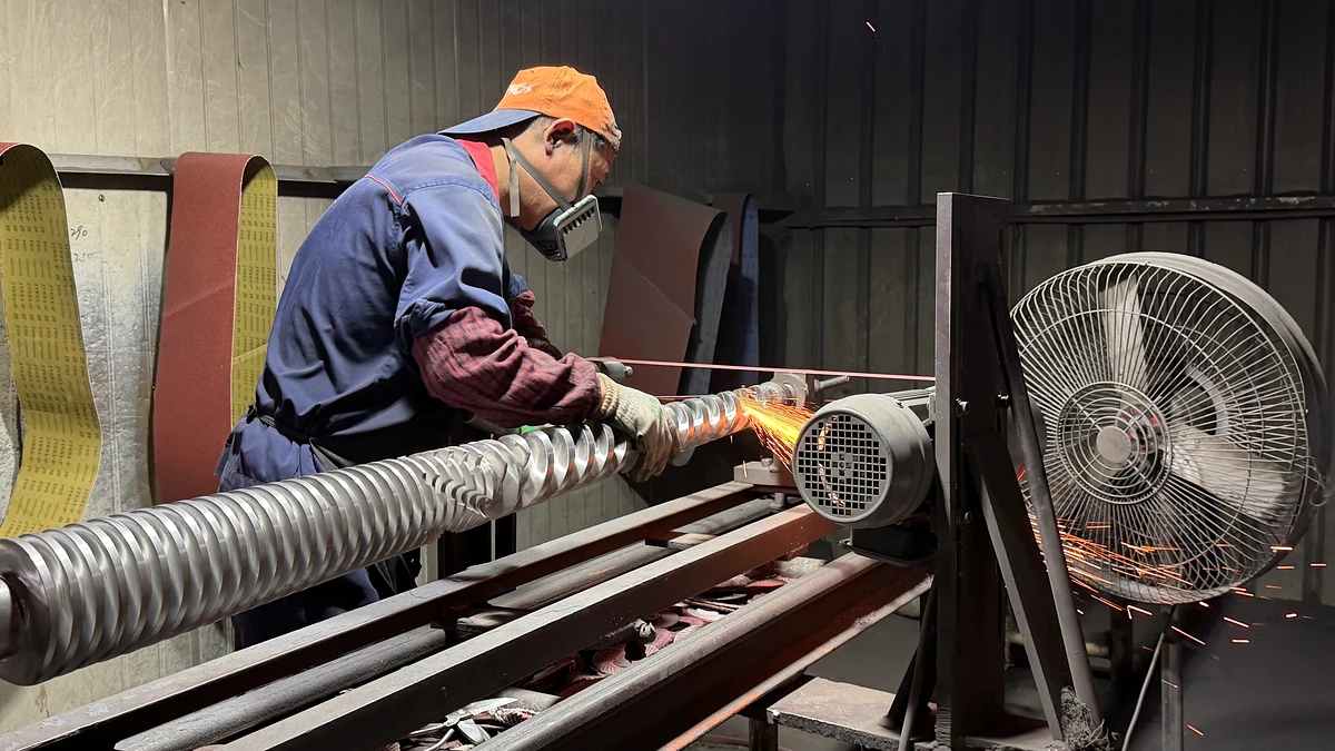 Worker finishing a long extrusion screw with an abrasive belt in a workshop