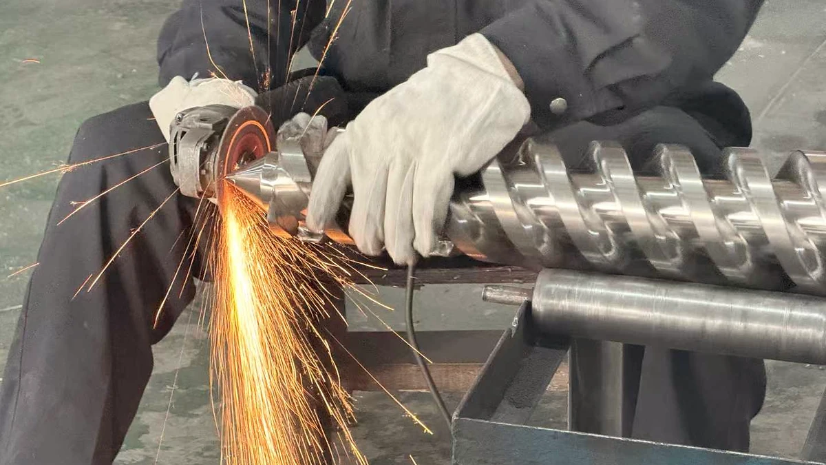 Worker grinding a screw flight with a handheld abrasive tool and visible sparks